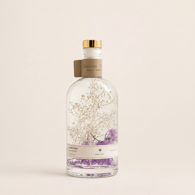A clear glass bottle with a gold cap and a kraft paper neck label, filled with dried baby's breath and purple flowers. The label at the bottom reads 'LAVENDER' and 'Delicate Herbs & Spices'.