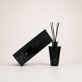A black reed diffuser bottle with four reeds next to its black rectangular box, both branded LIGHT ART, photographed on a clean off-white studio background.