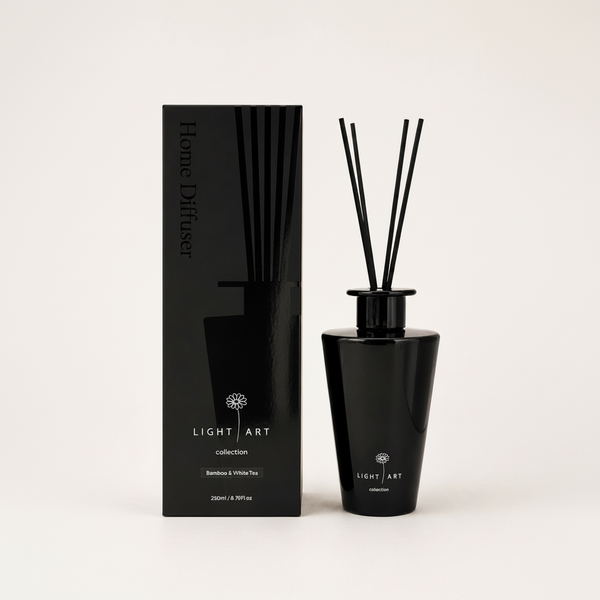 A black reed diffuser bottle with black reeds next to its black packaging box, both featuring the brand name 'Light Art' and the scent 'Bamboo & White Tea', on a light beige background.