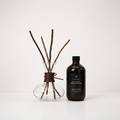 A reed diffuser set on a white background, featuring a clear glass bottle with a dark brown label reading 'Light Art' and 'Aroma Diffuser', next to a clear glass vase with brown reeds and a dark brown leather tie.