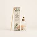 Light Art Botanical Home Diffuser set featuring a clear glass bottle with a gold cap, a decorative floral diffuser box, and two bamboo diffuser sticks on a warm off-white background.