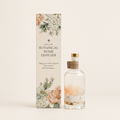 A botanical home diffuser bottle with a clear glass body, gold cap, and cork stopper stands beside its tall illustrated box. The packaging features cream floral artwork with green leaves and black text reading 'Light Art Botanical Home Diffuser.